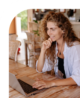 A smiling woman with long wavy hair works at a computer