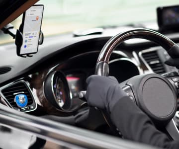 The driver in gloves holds the steering wheel, and a holder with a smartphone, which displays an application for taxi drivers, is fixed on the windshield.